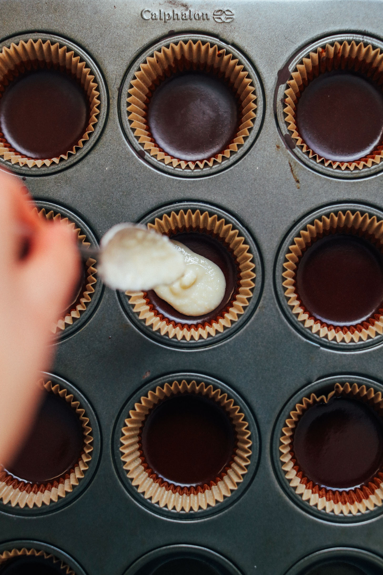 Pouring a layer of coconut butter over dark chocolate in parchment lined muffin cups