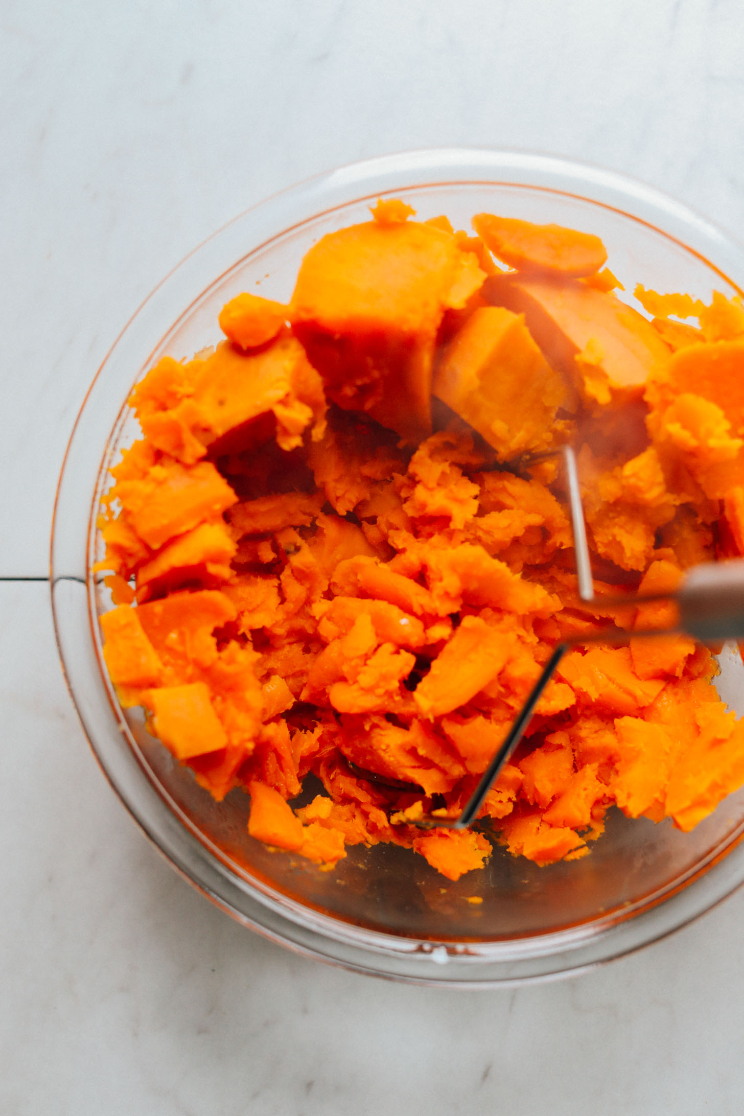 Using a potato masher to lightly mash bright orange sweet potatoes
