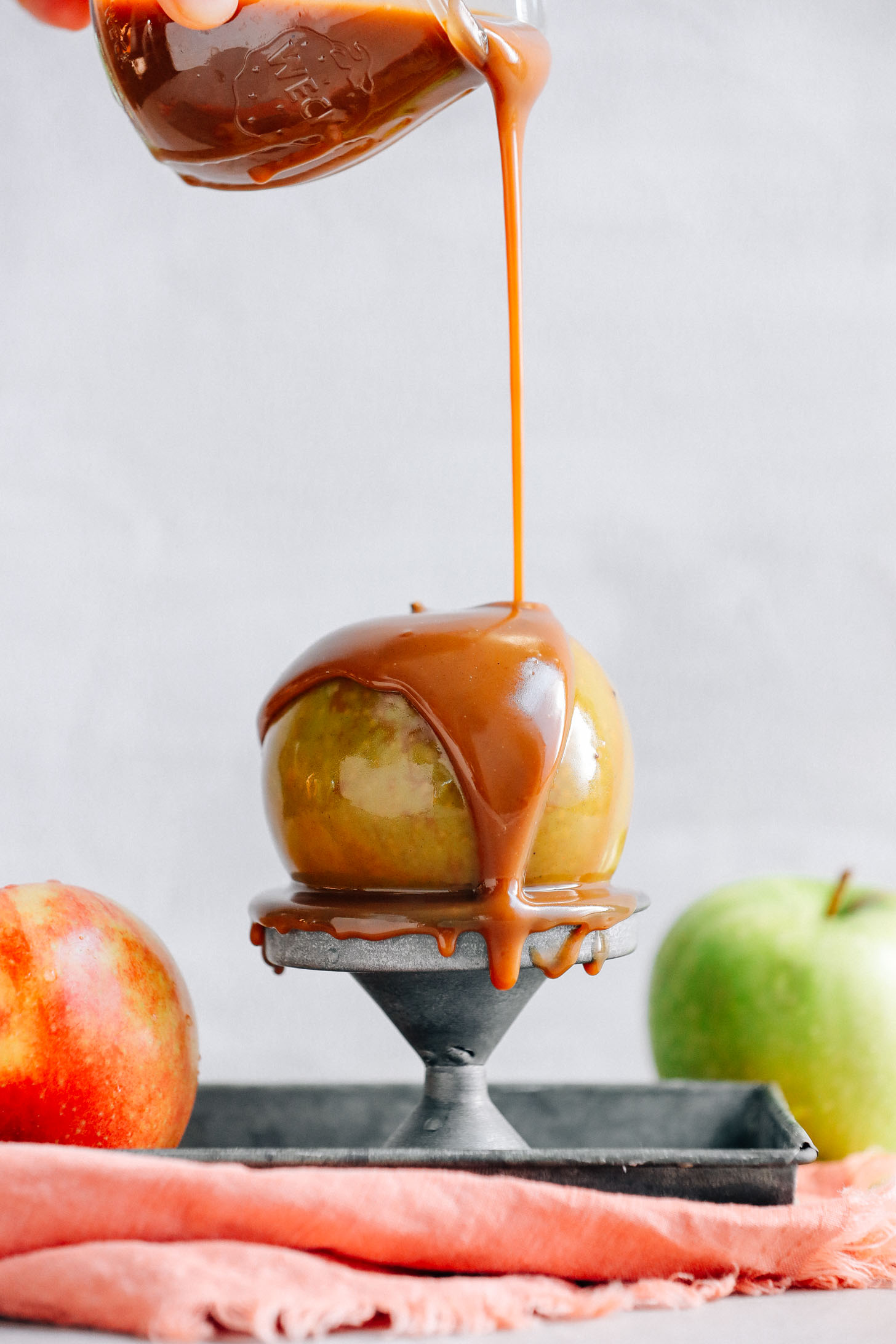 Drizzling our AMAZING Vegan Caramel Sauce onto an apple perched on a metal stand