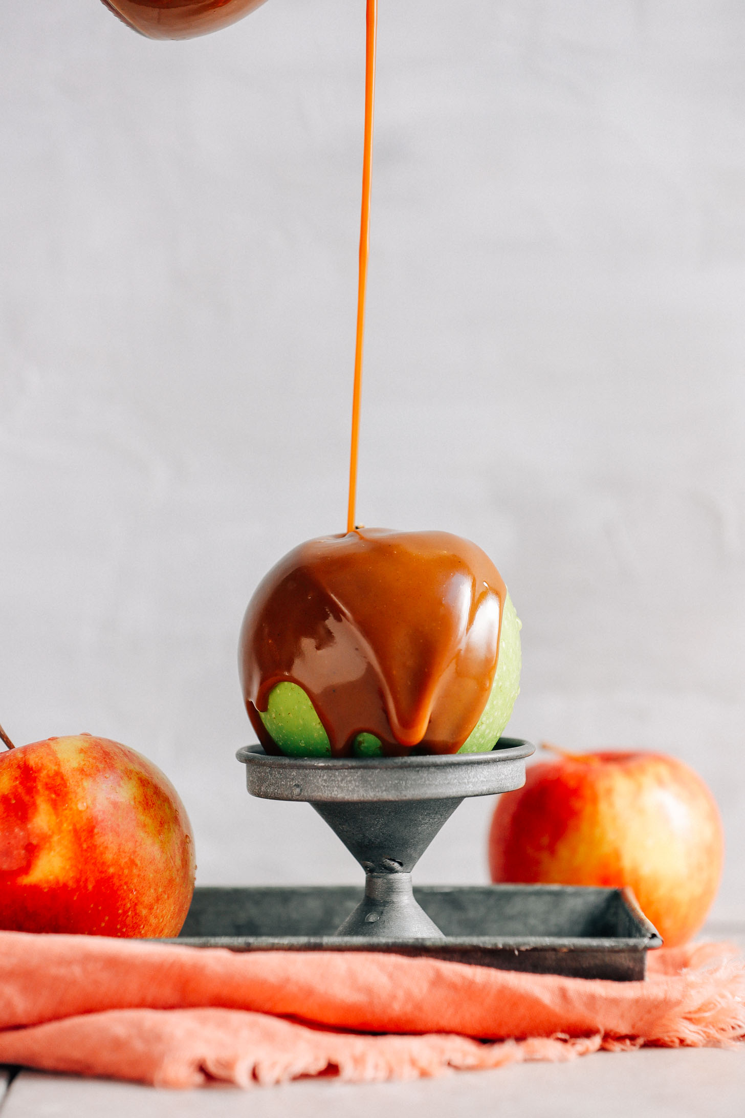Close up shot drizzling Vegan Caramel Sauce onto a green apple perched on a metal stand