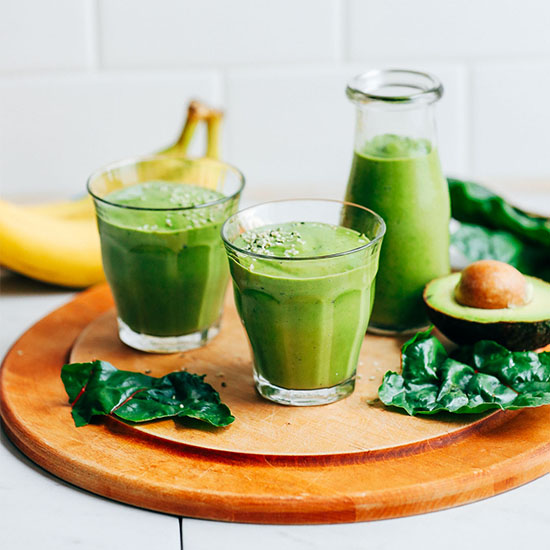 Glasses and a jar of our Avocado Green Smoothie alongside ingredients used to make it