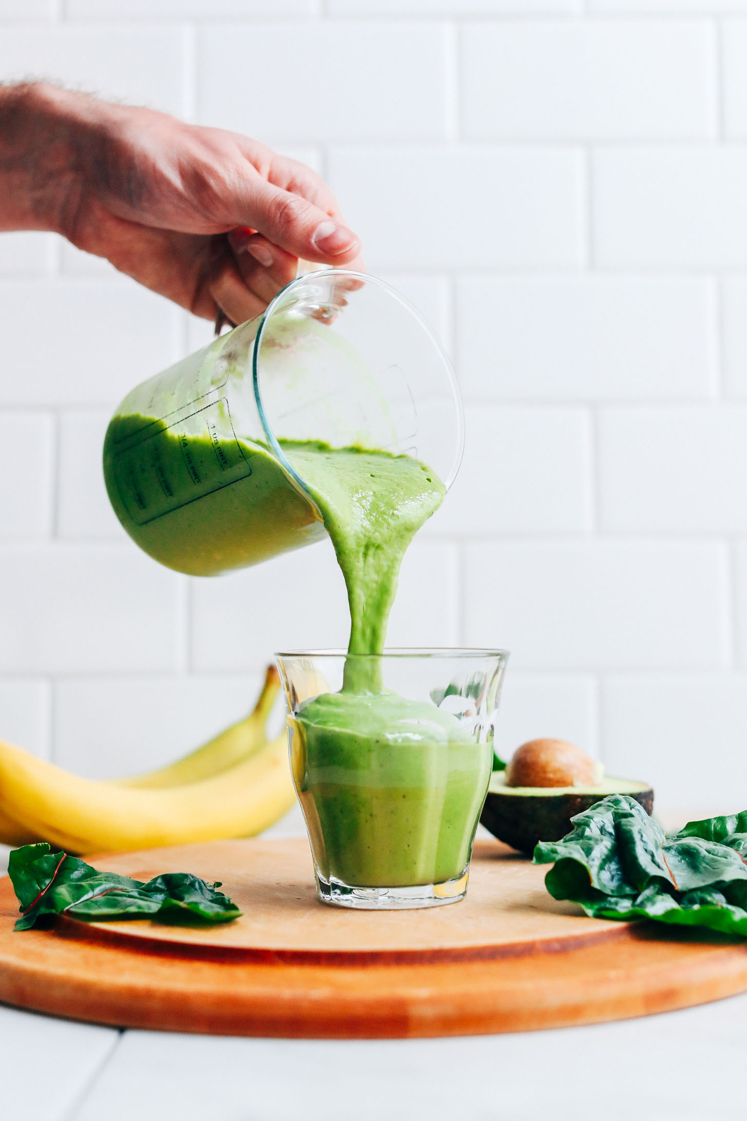 Pouring a glass of Creamy Avocado Green Smoothie for a plant-based snack