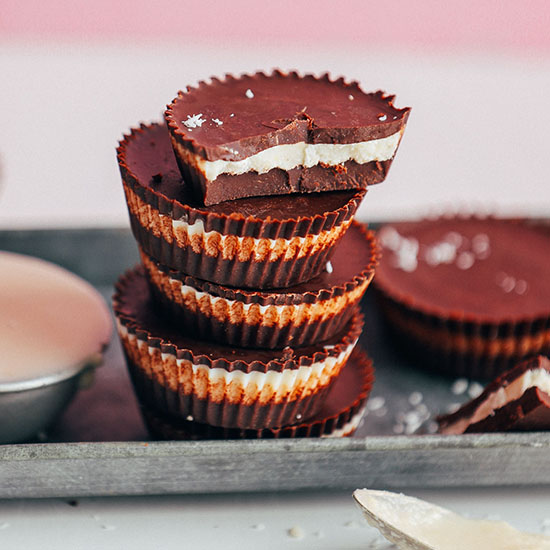 Stack of homemade Vegan Coconut Butter Cups on a tray with a measuring cup of coconut butter