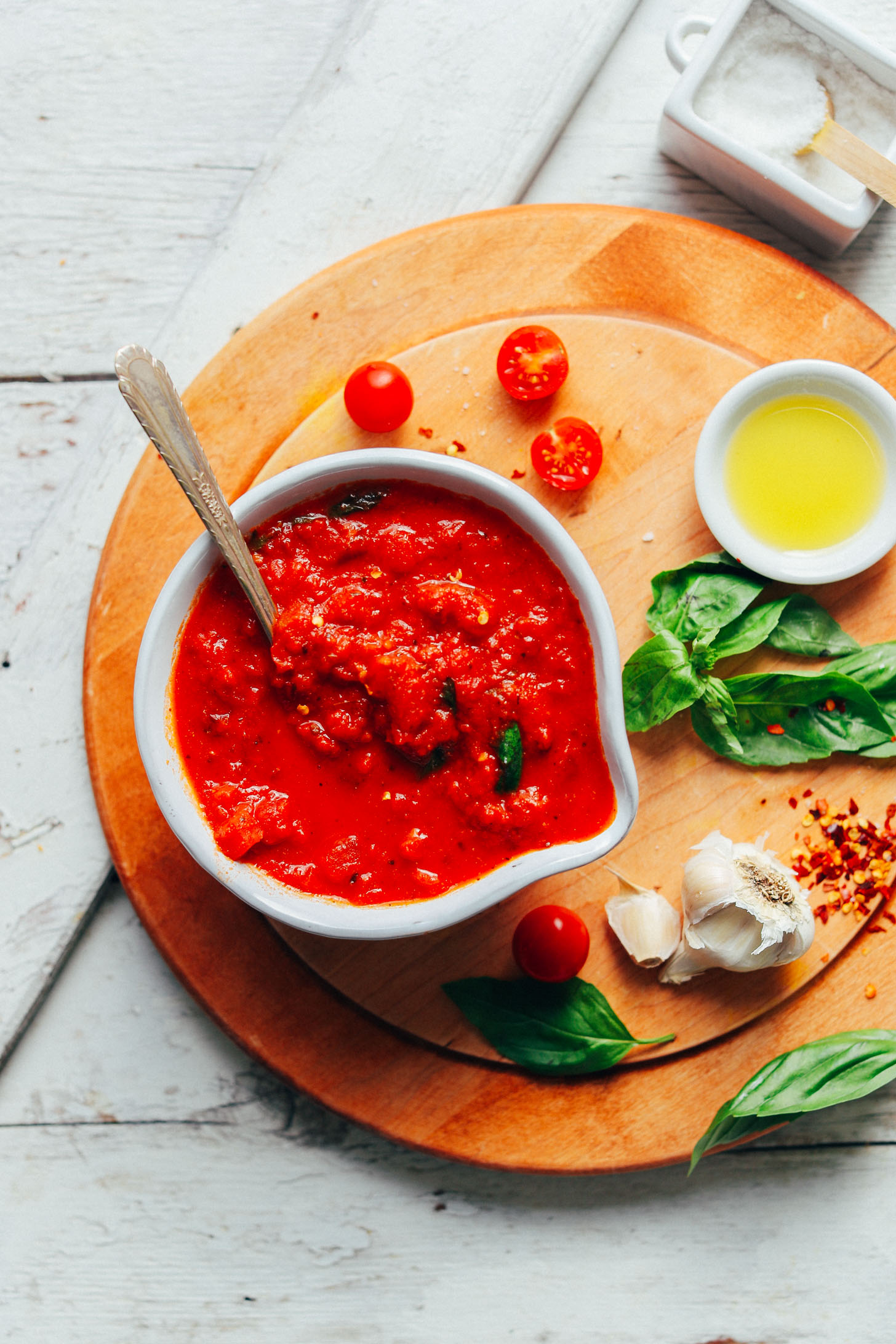 Bowl of our EASY 1-Pot Marinara Sauce on a cutting board with fresh basil, tomatoes, garlic, red pepper flakes, and olive oil