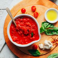 Cutting board with a bowl of homemade marinara beside ingredients used to make it