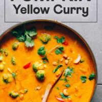 Wooden spoon in a large rimmed skillet filled with vegan pumpkin curry