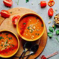 Two bowls of Romesco Soup surrounded by ingredients used to make it
