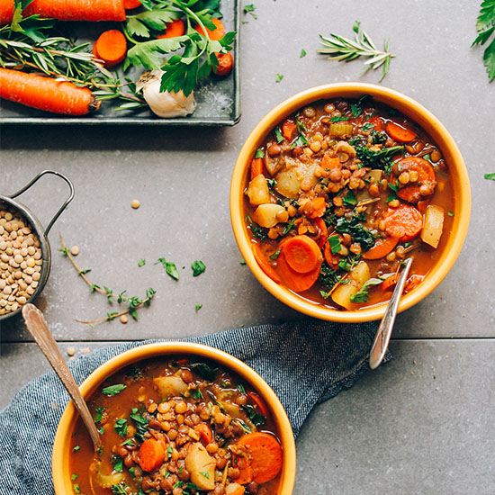 Ciotole di zuppa di lenticchie vegana quotidiana accanto a un vassoio di verdure