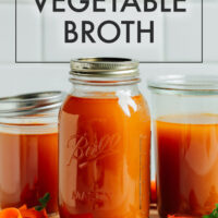 Jars of homemade vegetable broth on a cutting board