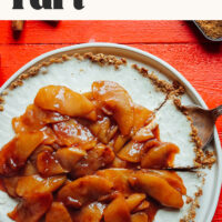 Plate with a cheesecake tart with text above it saying vegan + gluten-free caramel apple cheesecake tart