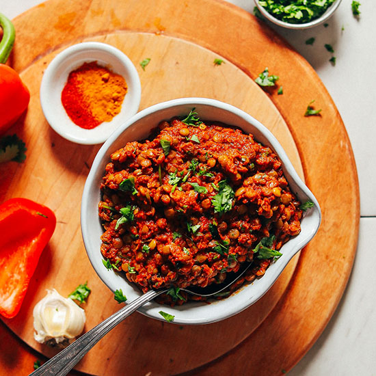 Bowl of Moroccan-Spiced Lentils alongside vegetables and spices used to make it