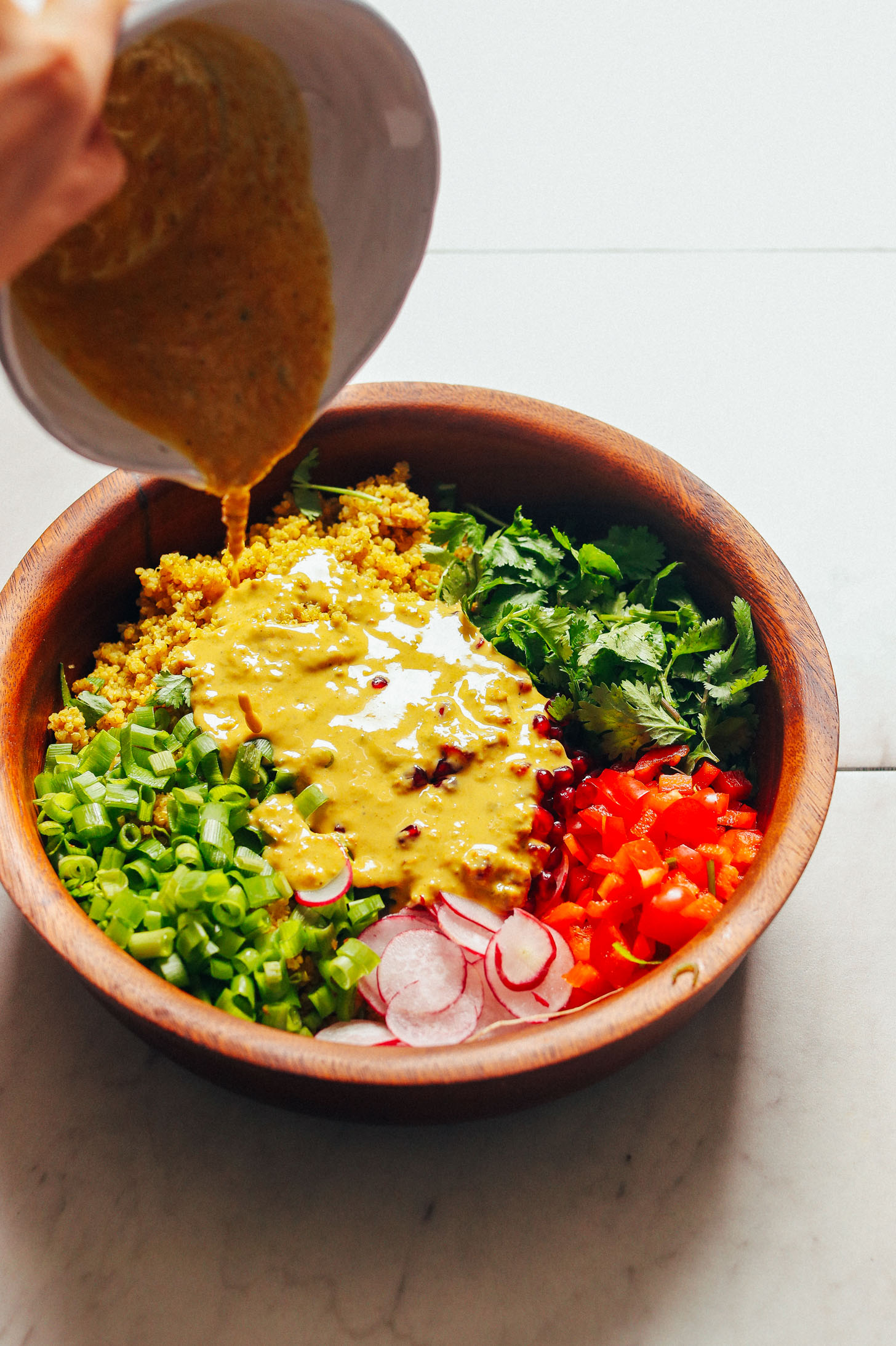 Pouring creamy curry dressing onto a big salad bowl filled with gluten-free Curried Quinoa Salad with vegetables