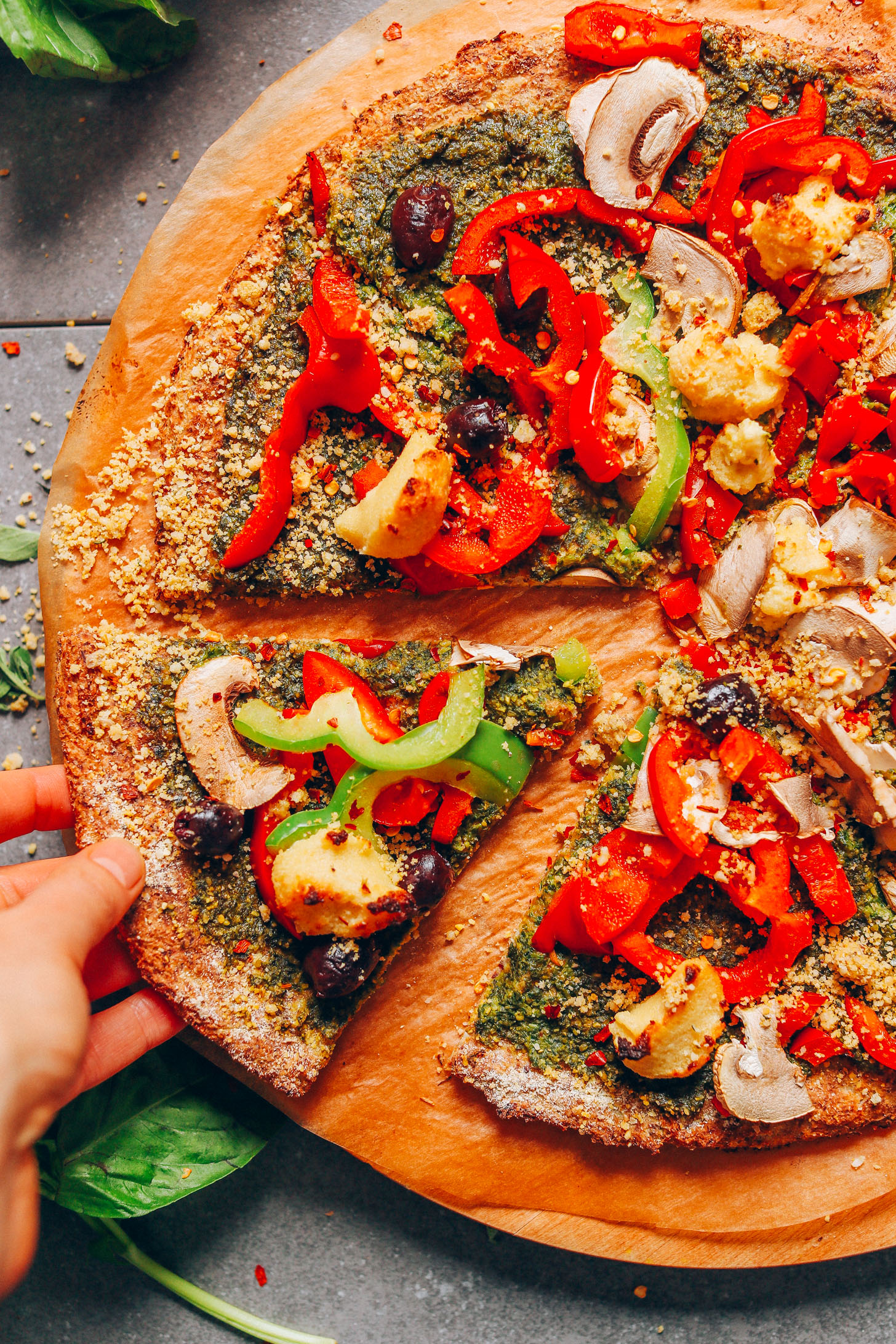 Picking up a slice of pizza topped with fresh vegetables and made using our vegan Gluten-Free Cauliflower Pizza Crust recipe