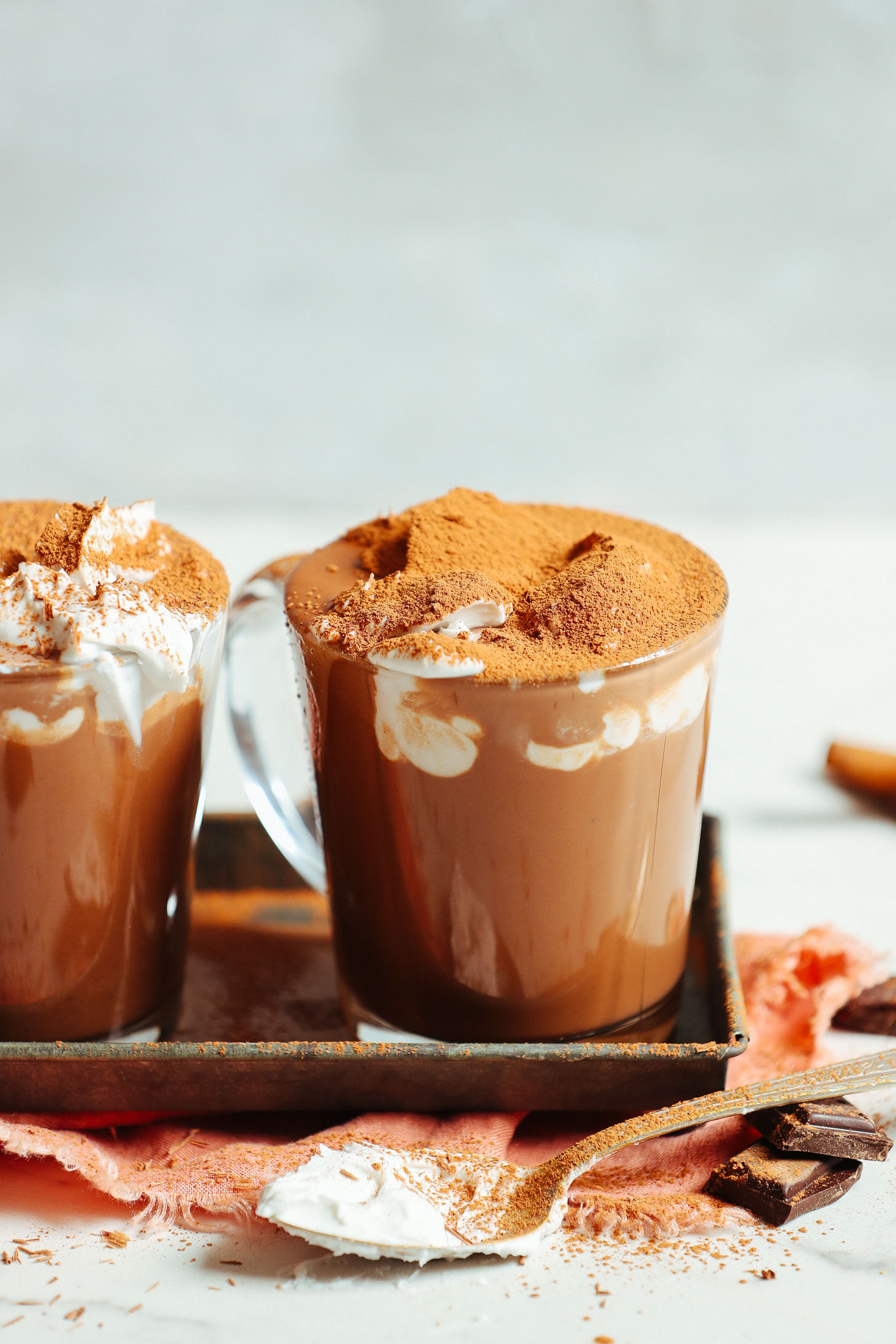 Mugs of Vegan Hot Chocolate topped with coconut whipped cream and shaved chocolate