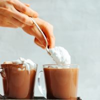 Spooning coconut whipped cream onto Vegan Hot Chocolate