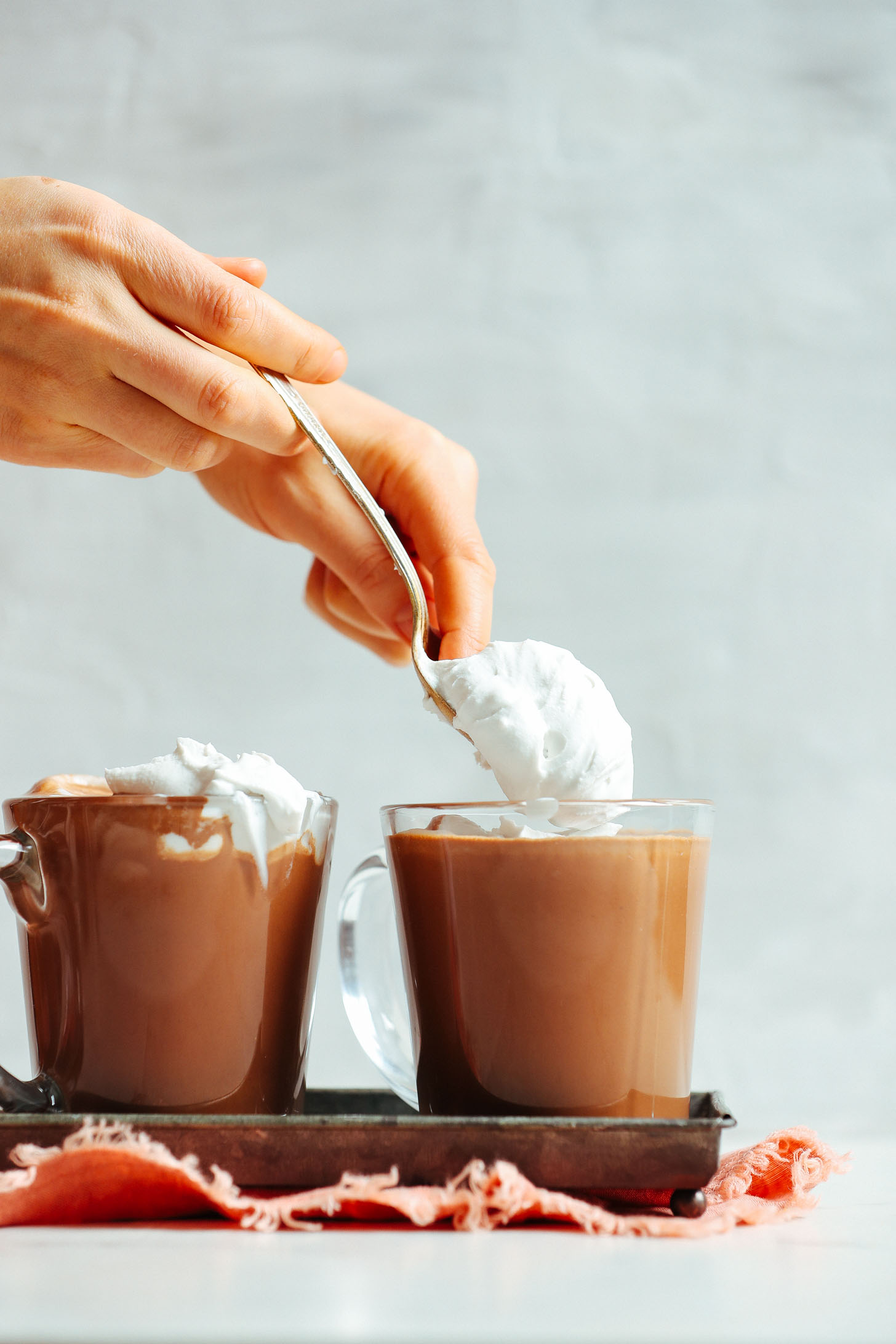 Spooning coconut whipped cream onto Vegan Hot Chocolate