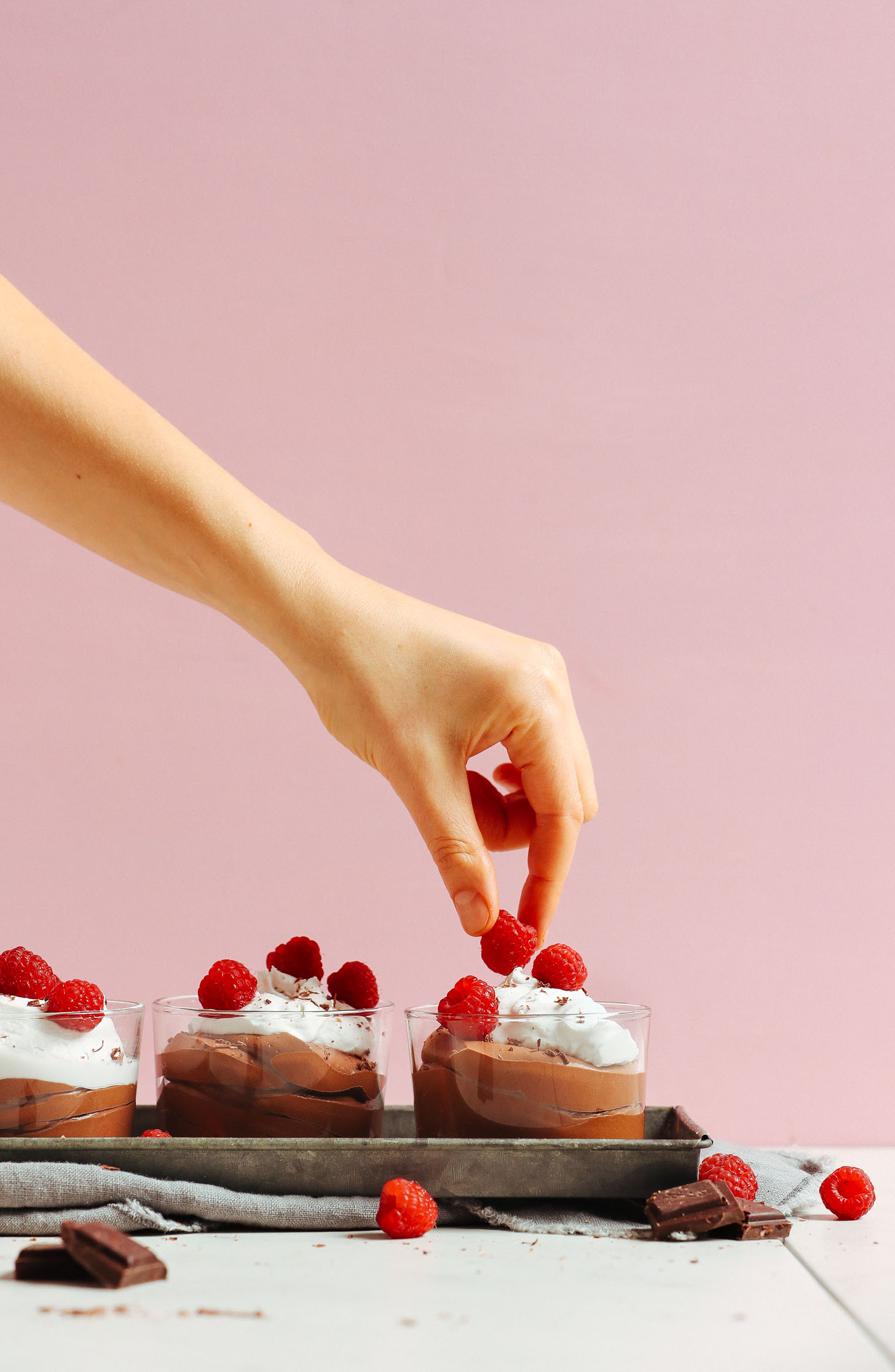 Placing a raspberry on top of a glass of Vegan Chocolate Mousse with coconut whipped cream