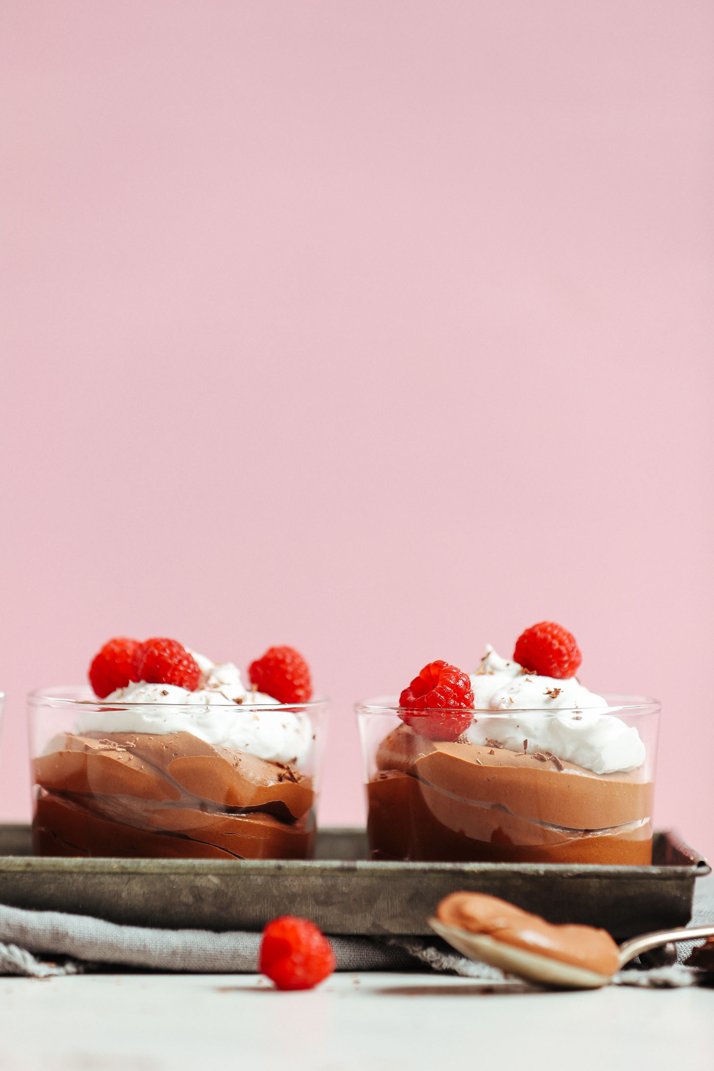 Two glasses filled with Naturally Sweetened Vegan Chocolate Mousse and topped with coconut whipped cream, fresh raspberries, and shaved chocolate