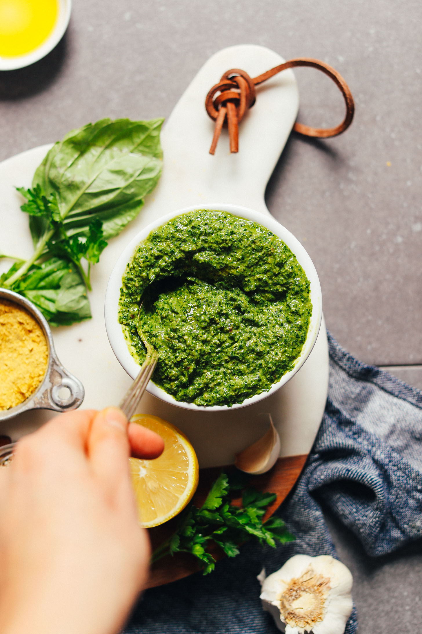 A bowl full of vibrant Super-Green Vegan Pesto surrounded by garnishes such as fresh basil and lemon