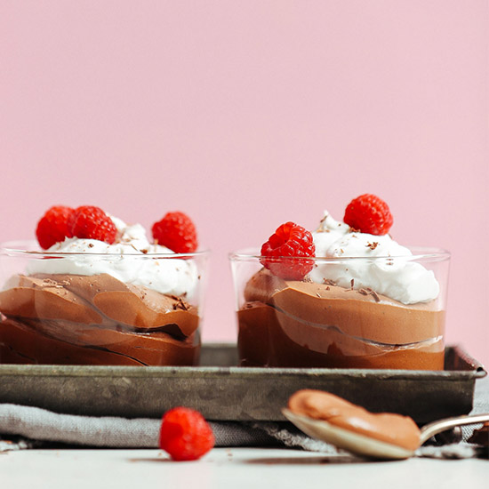 Tray holding two short glasses of Vegan Chocolate Mousse topped with coconut whip and raspberries