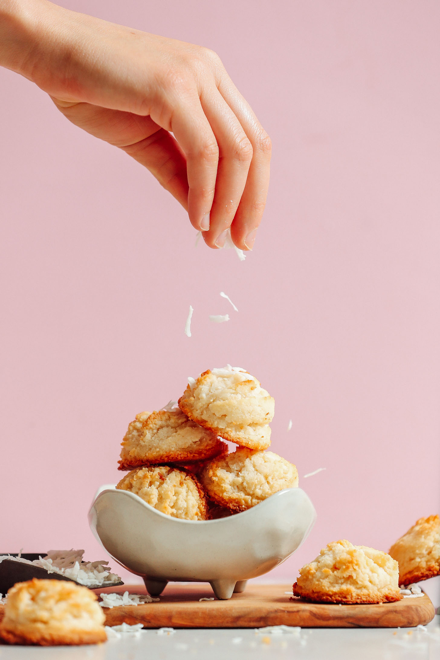 Sprinkling shredded coconut onto a stack of Vegan Coconut Snowball Cookies