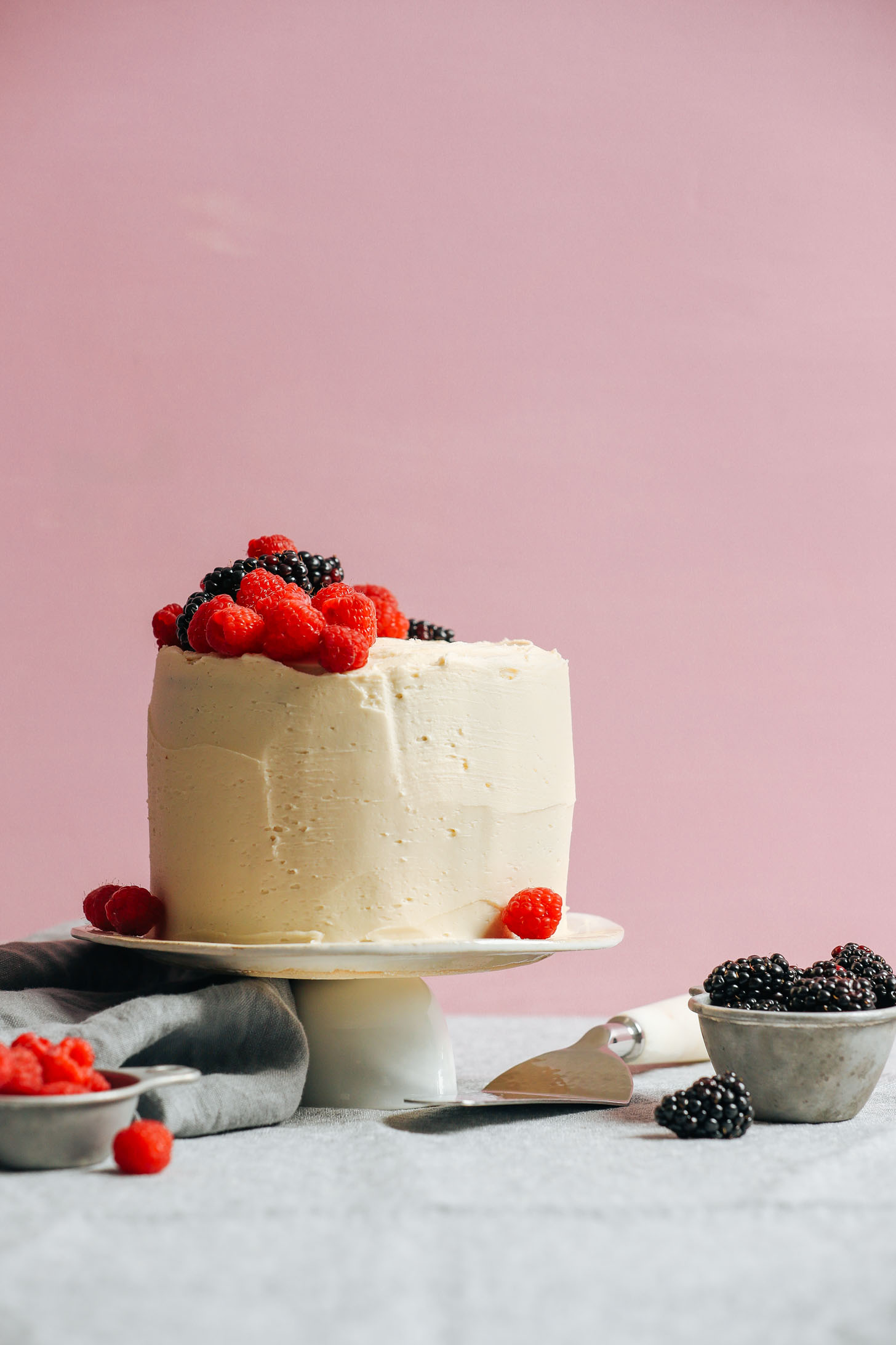 Our perfectly frosted 1-Bowl Vegan Gluten-Free Vanilla Cake perched atop a serving platter and decorated with fresh berries