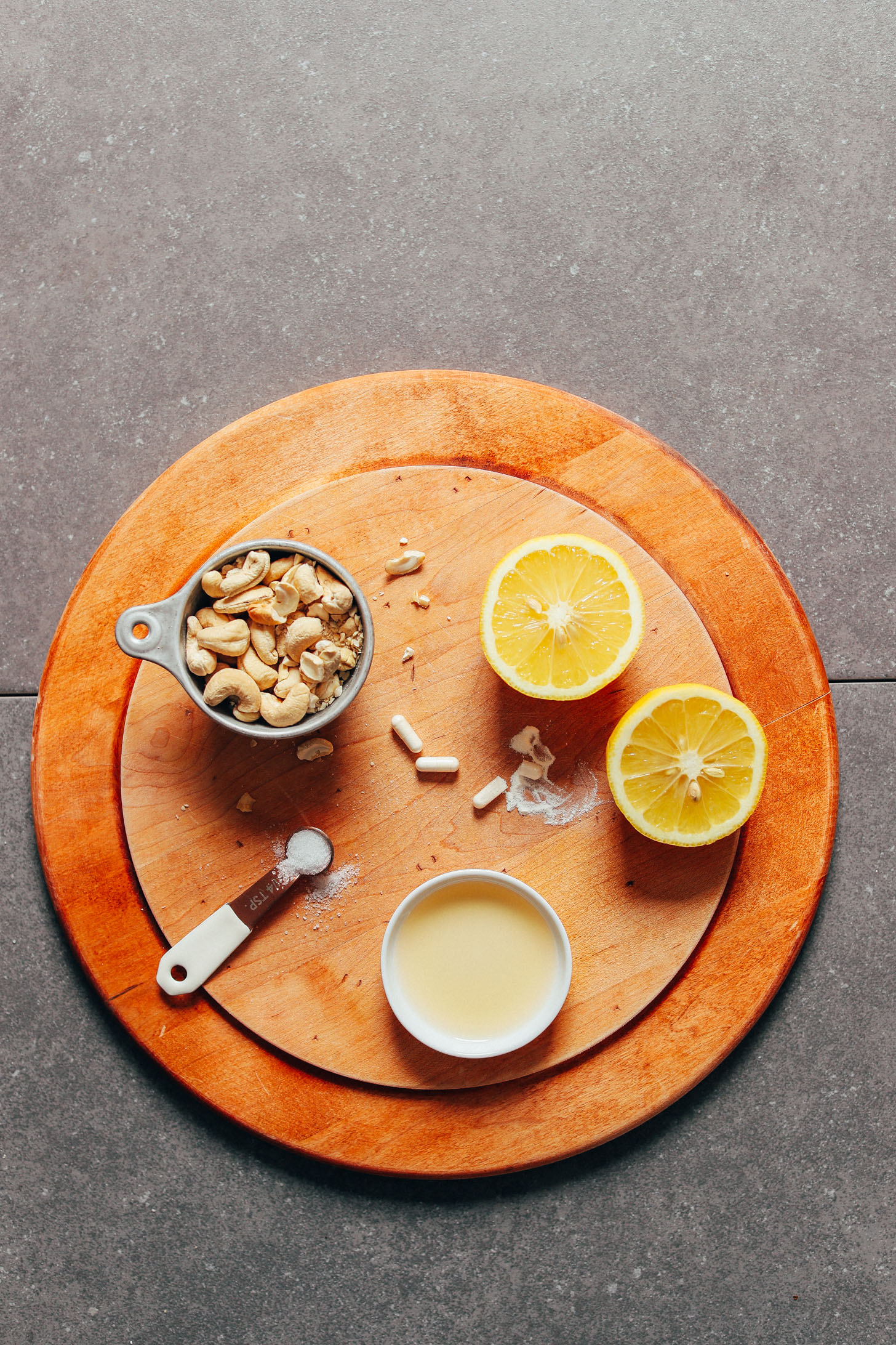 Wood cutting board with cashews, lemon, olive oil, probiotics, and salt for making homemade Vegan Sour Cream
