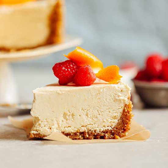 Slice of no-bake vegan coconut yogurt cheesecake topped with raspberries and orange peel