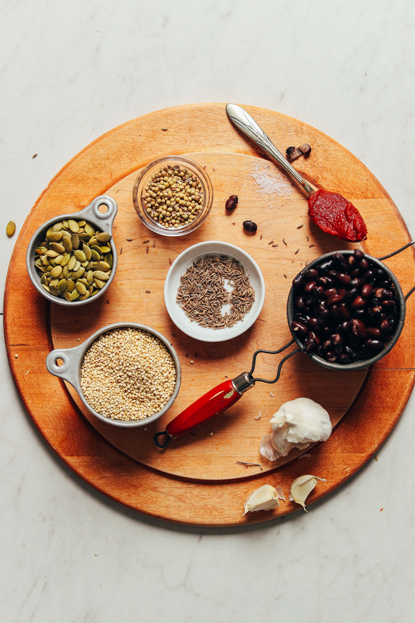 Pumpkin seeds, quinoa, garlic, black beans, and spices displayed on a cutting board for making Black Bean Quinoa Falafel