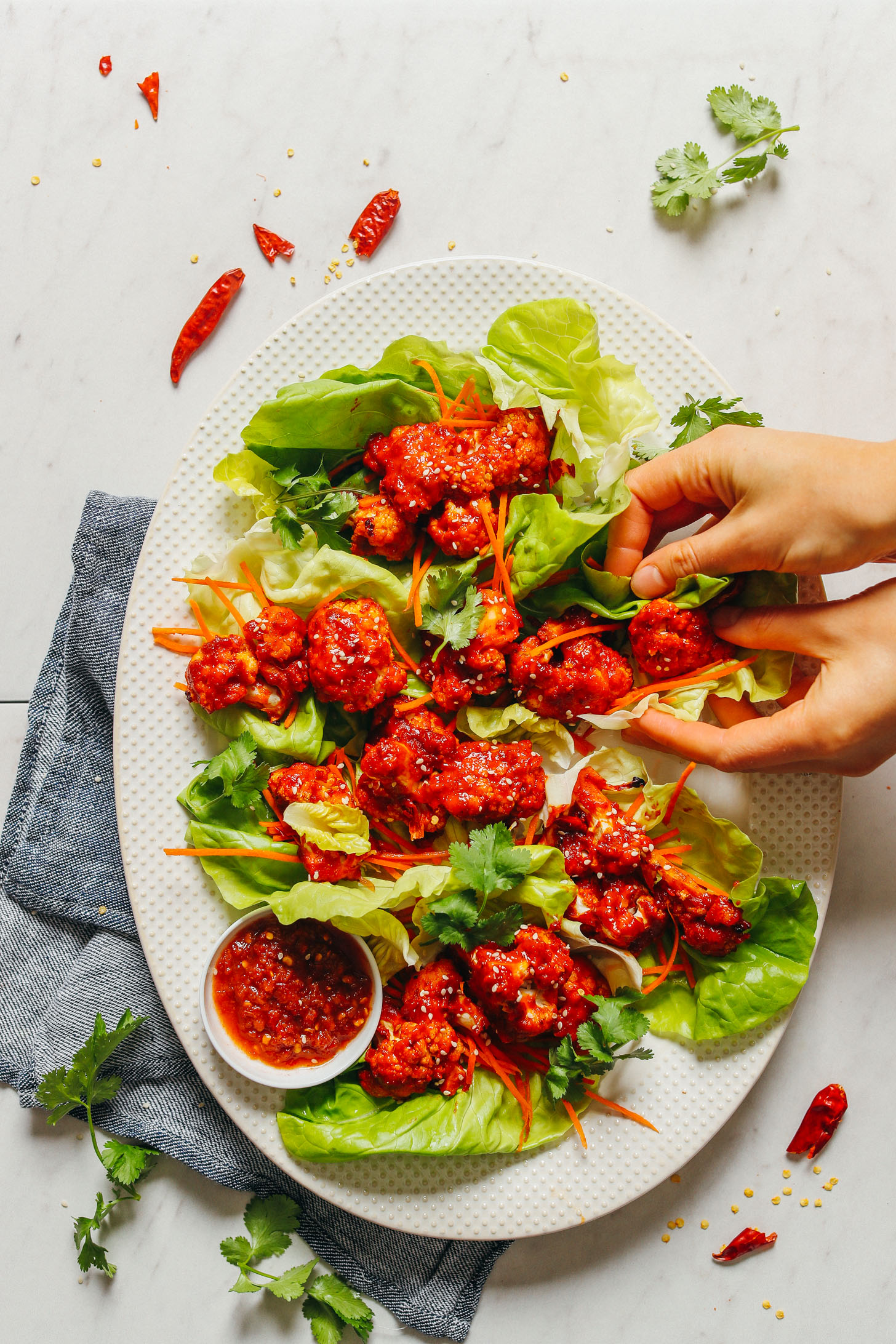 Large serving platter filled with Korean-Spiced Cauliflower Wings and shredded carrots in butter lettuce leaves