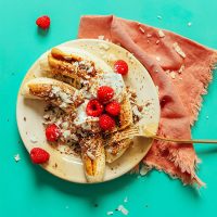 Plate with two Raw Banana Splits topped with nut butter, raspberries, and more