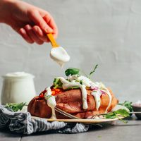 Using a spoon to drizzle homemade Vegan Sour Cream over a baked sweet potato