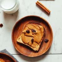 Slice of gluten-free toast smothered with delicious Cinnamon Raisin Peanut Butter for a healthy plant-based breakfast