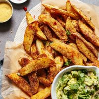 Parchment-lined platter filled with Oil-Free Baked Cheesy Fries and a bowl of guacamole