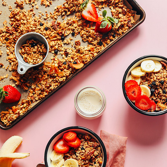 Bowls and baking sheet of homemade Vegan Oil-Free Granola topped with fresh fruit