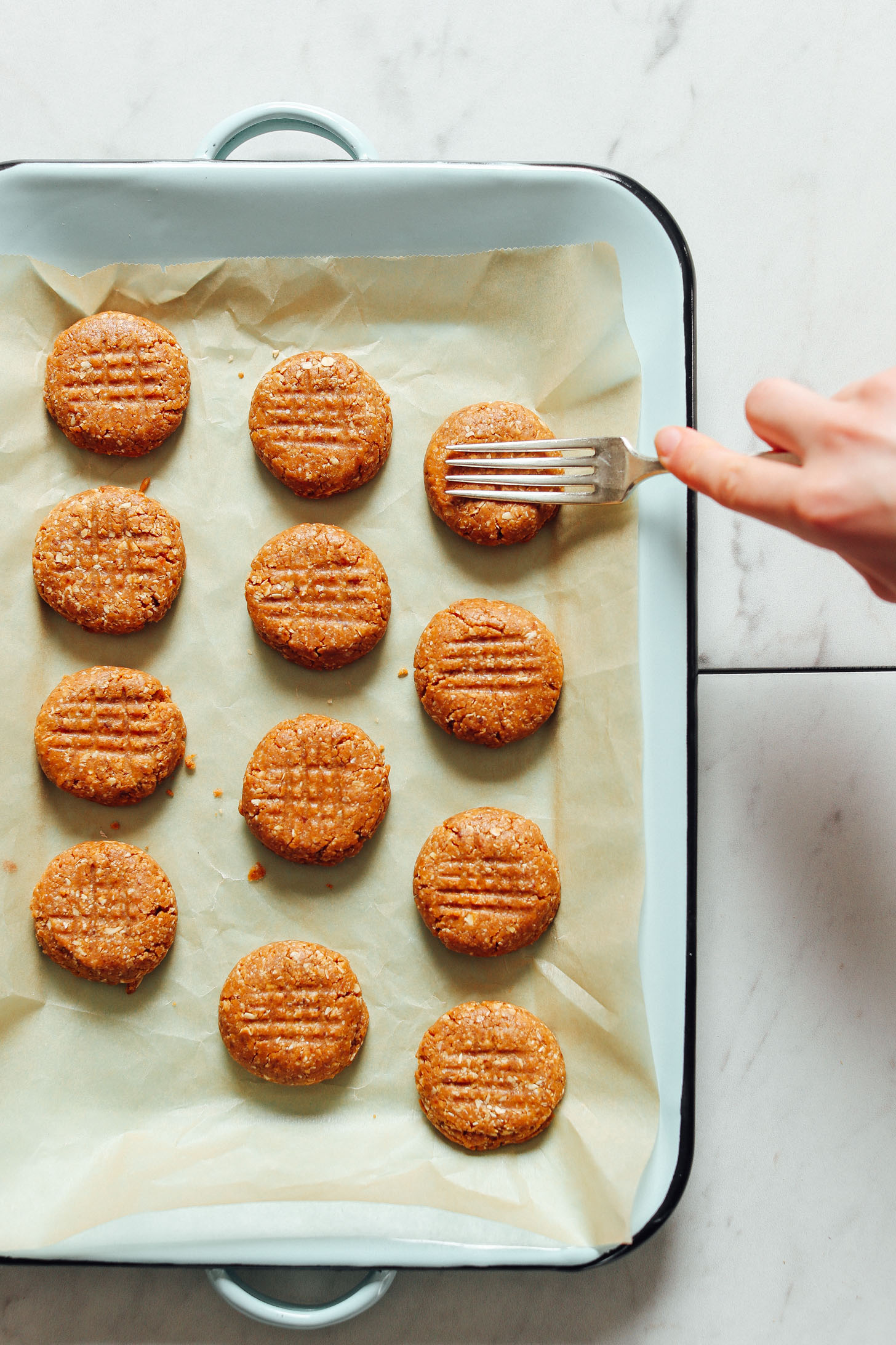 Using a fork to create a lattice design on top of a batch of our Peanut Butter Cookies recipe