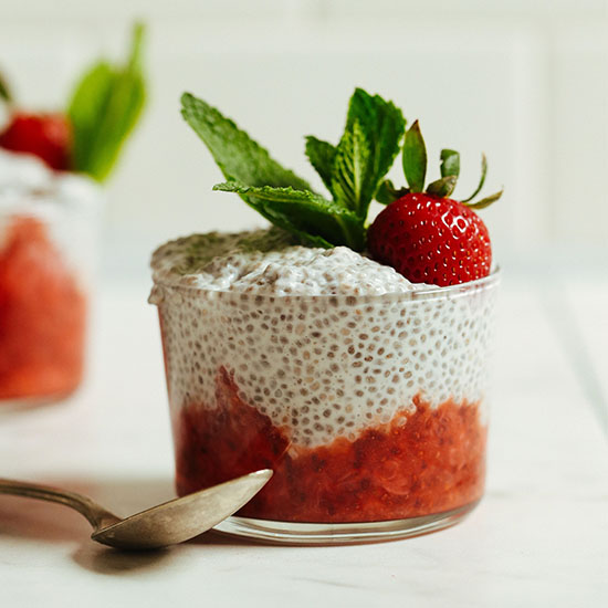 Short glass filled with fruit compote and Chia Pudding topped with a strawberry and mint leaves