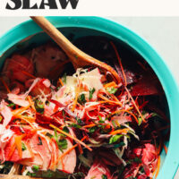 Using wooden tongs to toss a bowl of our super cleansing slaw recipe