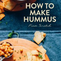 Using a spoon and a pita chip to pick up homemade hummus from a bowl