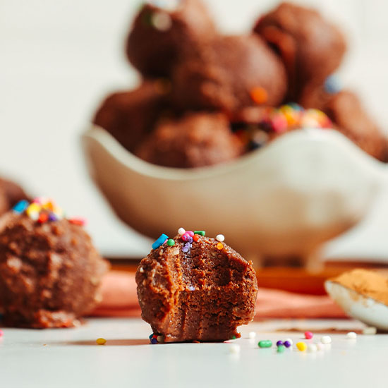 Partially eaten Vegan Chocolate Cake Bite topped with sprinkles in front of a bowl with more cake bites