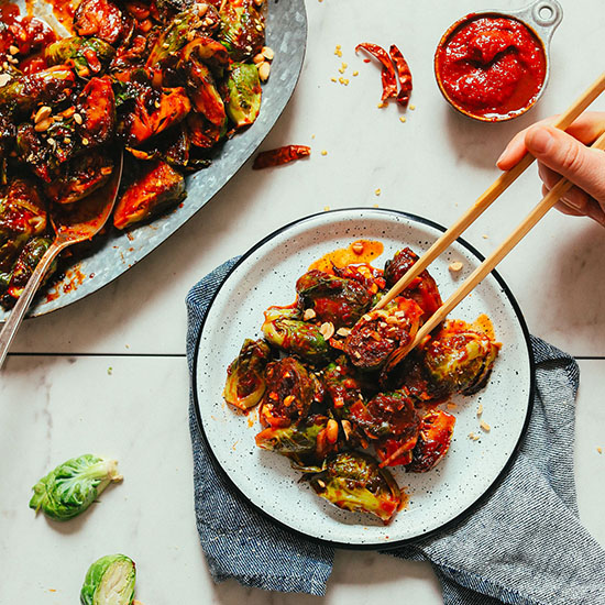 Using chopsticks to grab a bite of Gochujang Brussels Sprouts from a plate