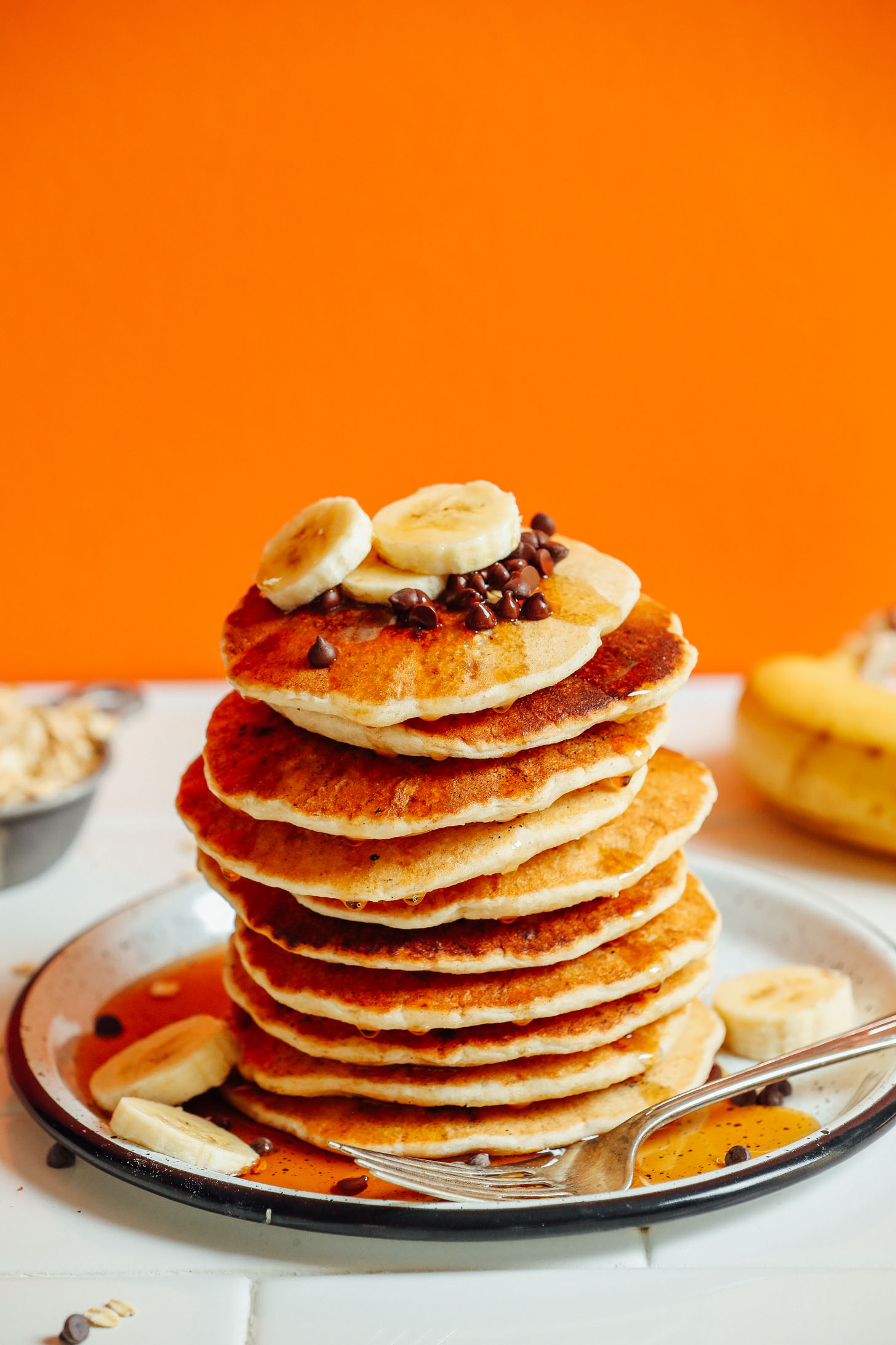 Tall stack of fluffy vegan Banana Oat Pancakes drizzled with maple syrup
