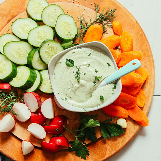 Bowl of Creamy Vegan Ranch dressing surrounded by fresh chopped vegetables for dipping