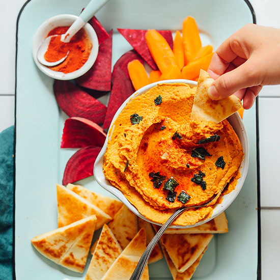 Dipping a slice of pita bread into a bowl of our Pumpkin Hummus recipe