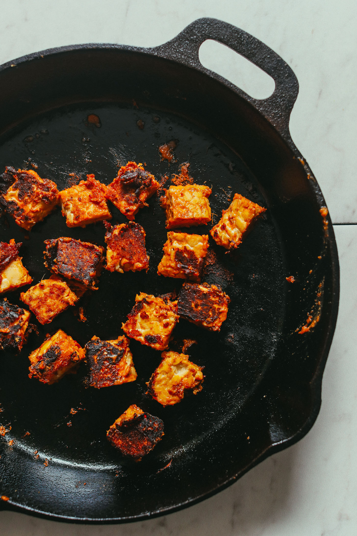 Overhead image of tempeh being stir fried in peanut sauce in a cast iron pan
