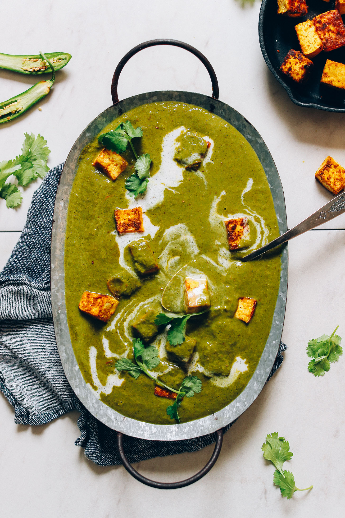 Overhead image of vegan palak paneer served in a metal tin with cubes of tofu and coconut milk garnish