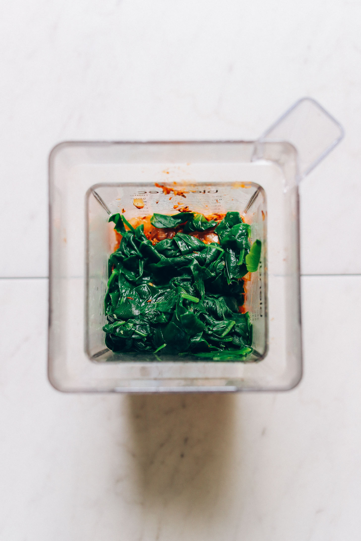 Overhead image of a blender with palak paneer ingredients and steamed spinach on top
