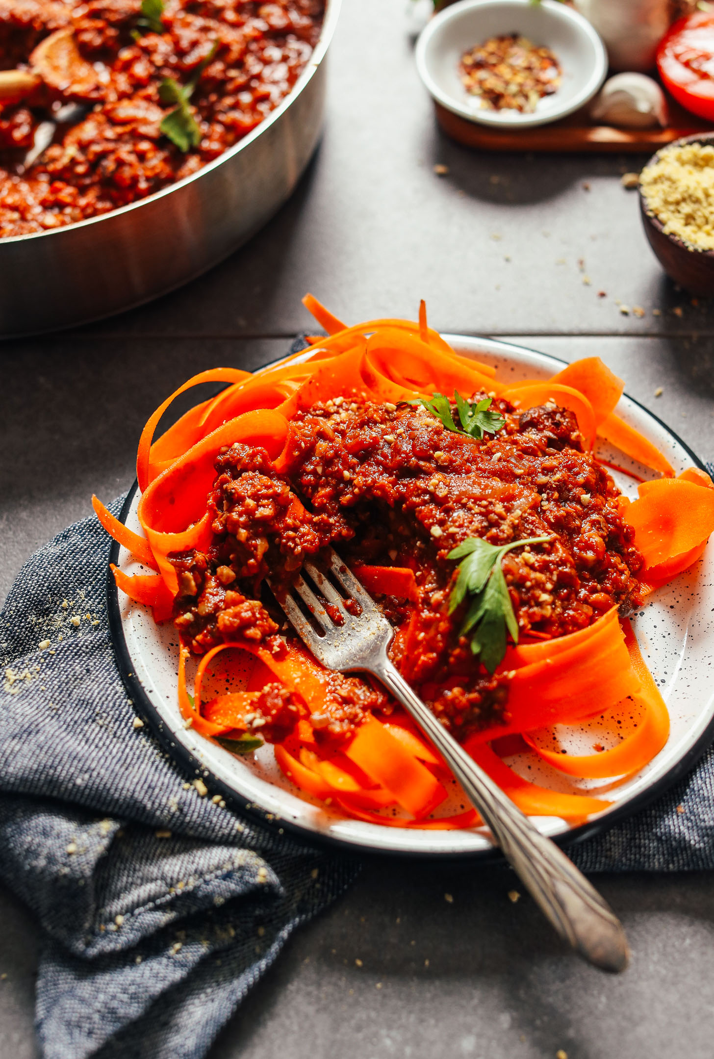 Image of tempeh bolognese over carrot noodles served on a white plate over a blue towel, garnished with parsley
