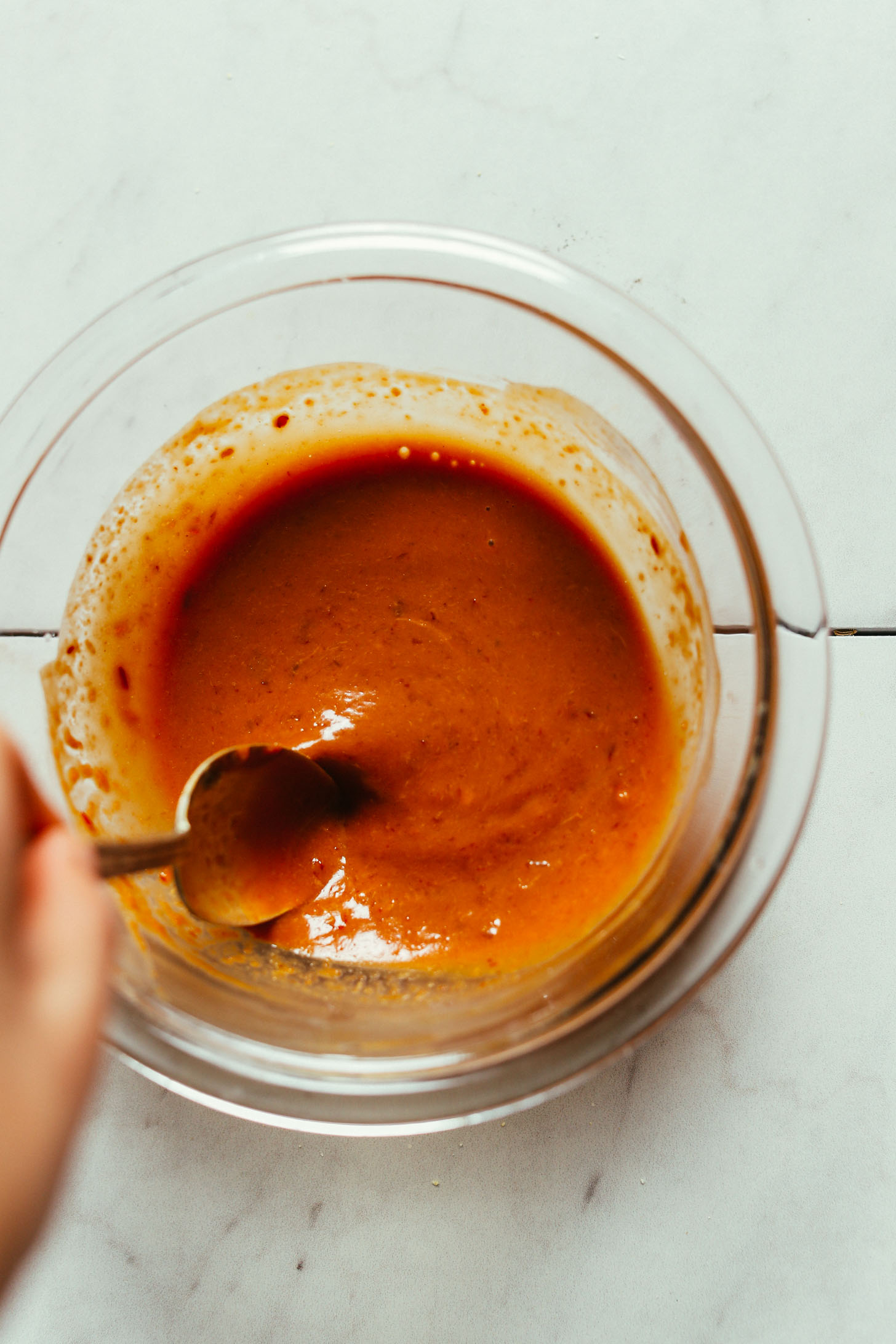 Using a spoon to stir a bowl of our homemade peanut sauce for making Peanut Tofu
