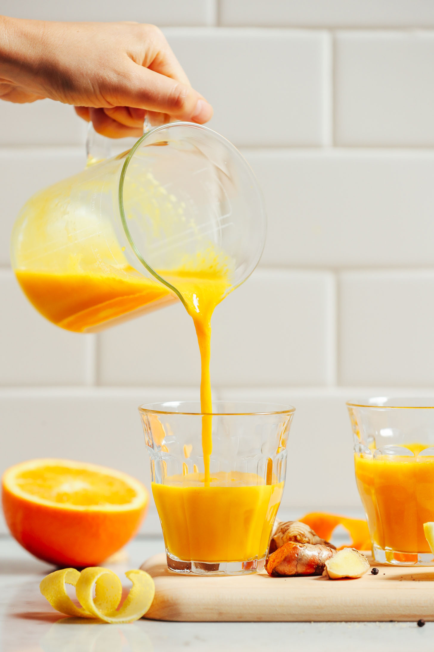 Pouring a batch of our Turmeric Wellness Shots recipe from a measuring glass into drinking glasses
